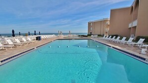 A swimming pool with lounge chairs and a building in the background. - Ocean Club North C208 (New Smyrna Beach)