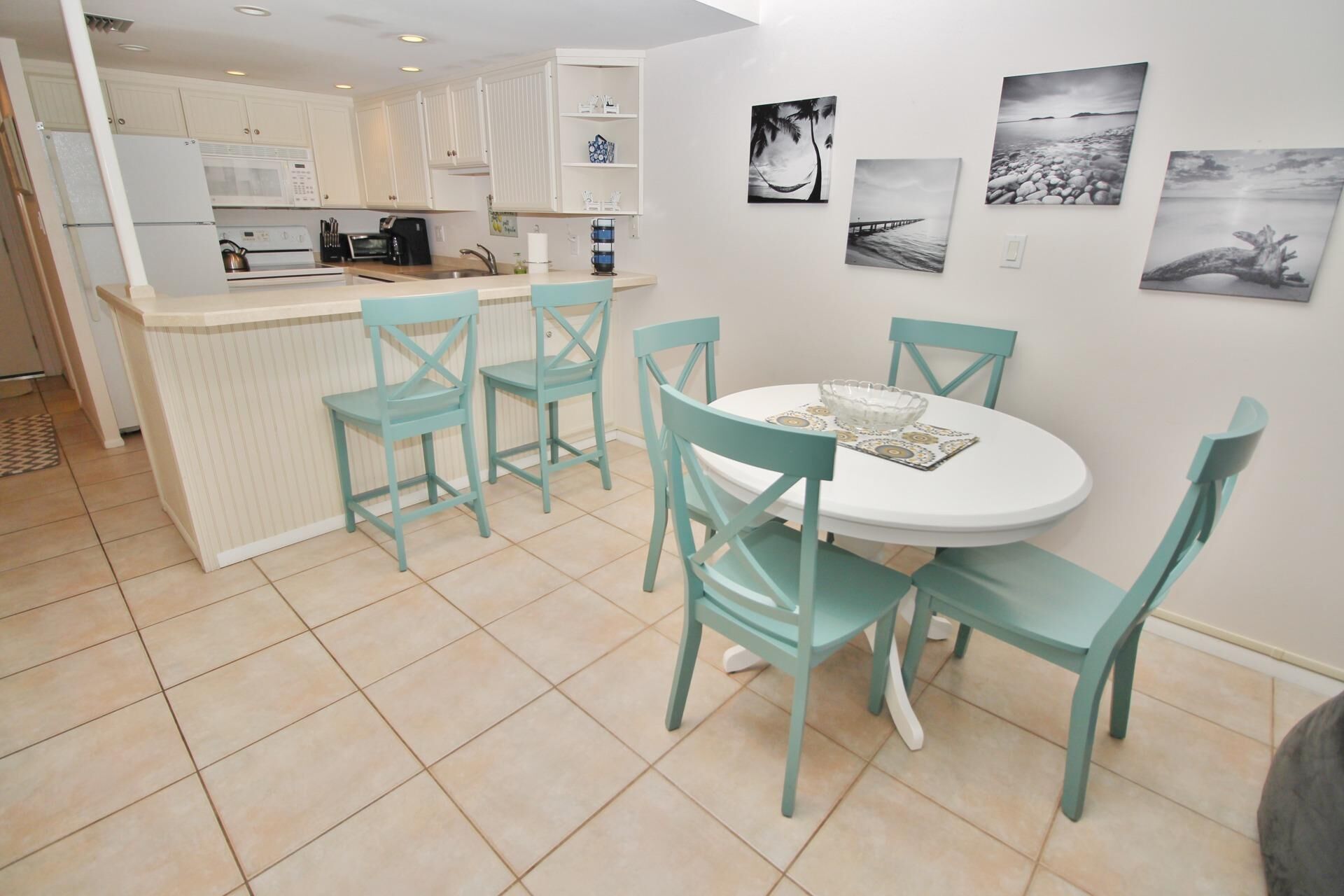 Una cocina moderna con armarios blancos, una isla central y un comedor con sillas color turquesa y una mesa blanca.