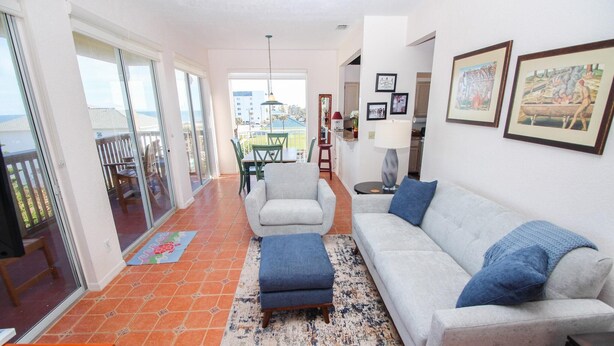 Un salon comprenant un canapé, un pouf et un coin repas avec des chaises et une table.
