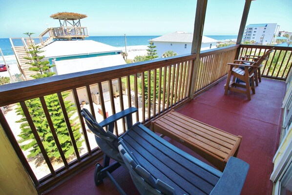 A balcony with wooden furniture, a view of the beach, and a building in the background. - Ocean Club at Turtle Mound 207 (New Smyrna Beach)