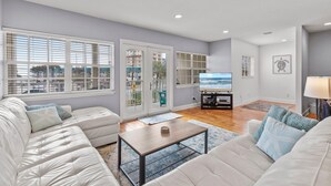 A spacious living room with a white sofa set, a coffee table, and a television. - Ocean's Edge (New Smyrna Beach)