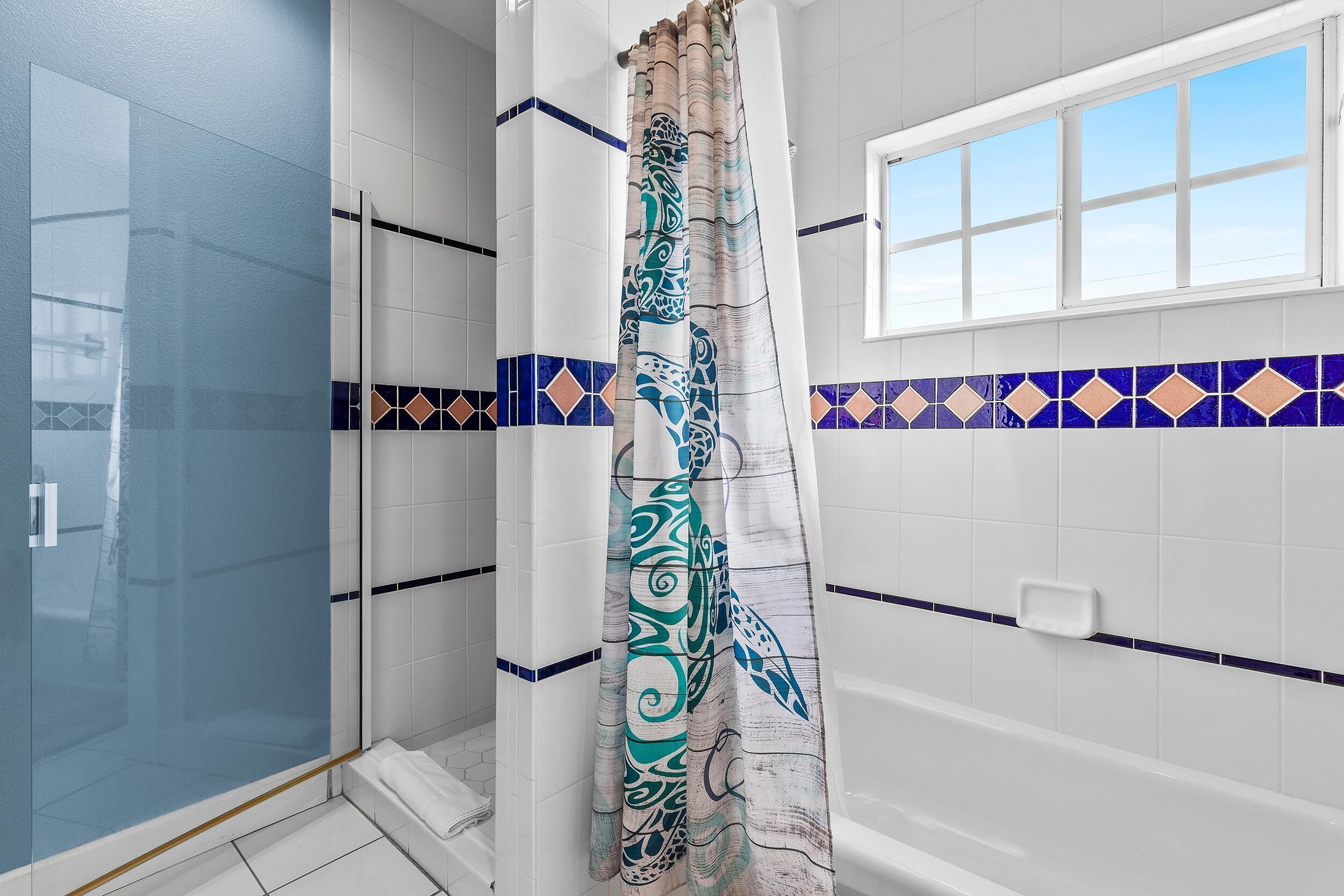 Un baño con cabina de ducha de vidrio, bañera y ventana.