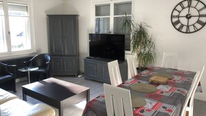 Una sala de estar con una mesa de madera oscura, un sofá, un televisor y un reloj en la pared.
