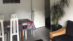 Una sala de estar moderna con comedor, un sofá, una planta en maceta y un cuadro en la pared.