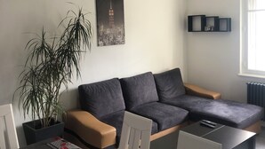 Una sala de estar moderna con un sofá seccional, una mesa de comedor con sillas, una planta en maceta y una obra de arte con un paisaje urbano en la pared.