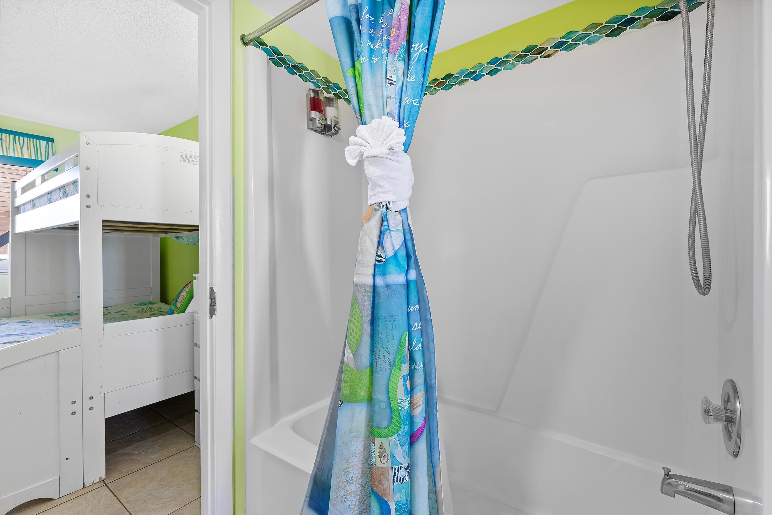 Une salle de bain avec un rideau de douche, une baignoire blanche et un lit superposé avec un matelas vert.