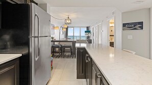 A modern kitchen with a black refrigerator, a marble countertop, and a view of the balcony. - Oceania Plaza 405 (New Smyrna Beach)