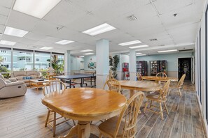 Amplio espacio interior con varias mesas y sillas de madera, una mesa de ping pong y vistas a un edificio.