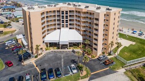A high-rise hotel with a central courtyard, parking area, and a view of the beach. - Oceania Plaza 405 (New Smyrna Beach)