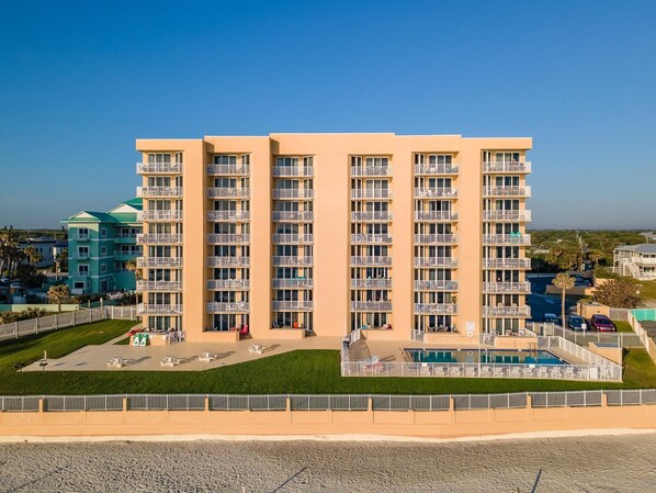 A multi-story hotel with balconies, a swimming pool, and a landscaped courtyard. - Oceania Plaza 502 (New Smyrna Beach)