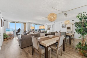 Ein geräumiger Wohnbereich mit großem Fenster zum Strand, einem Esstisch mit Stühlen und einer Sitzecke mit Sofas.
