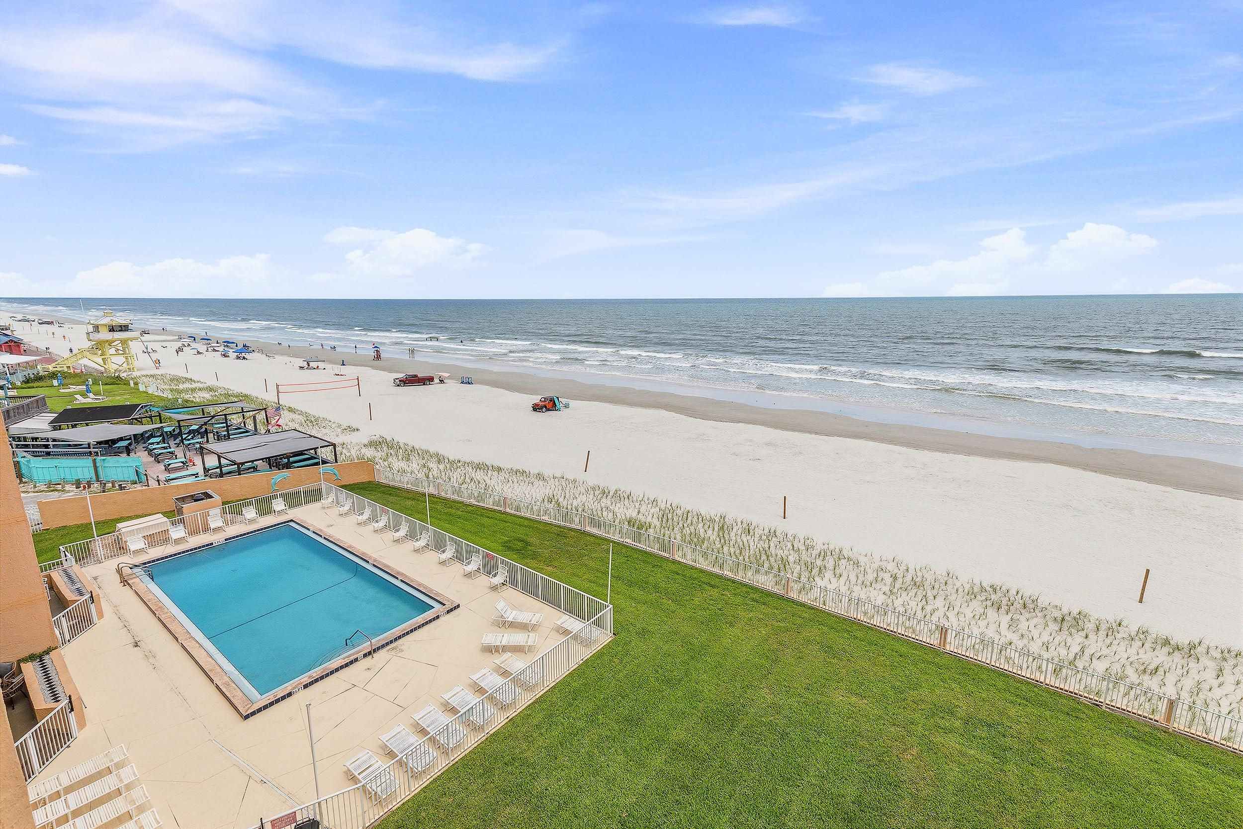 A beach view with a swimming pool, beach chairs, and umbrellas.