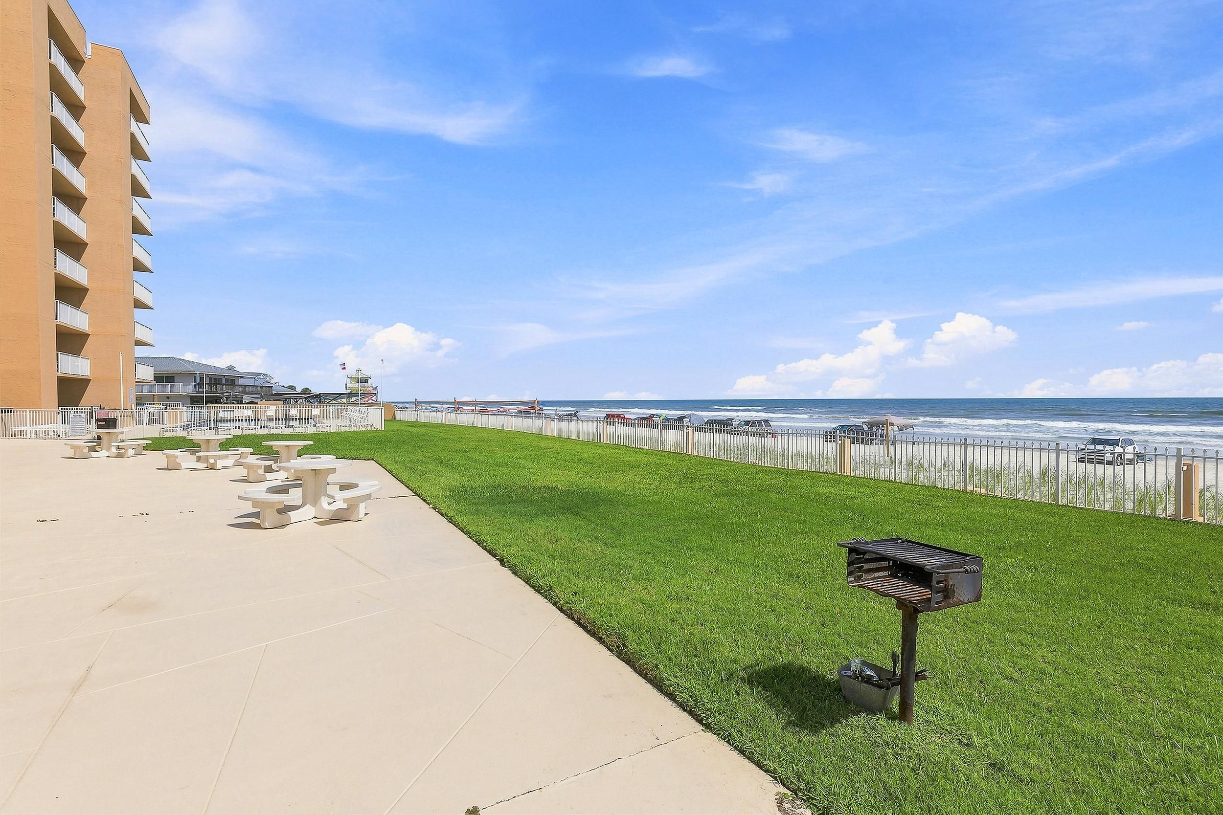 A beachfront promenade with a grassy area, picnic tables, and a view of the ocean.