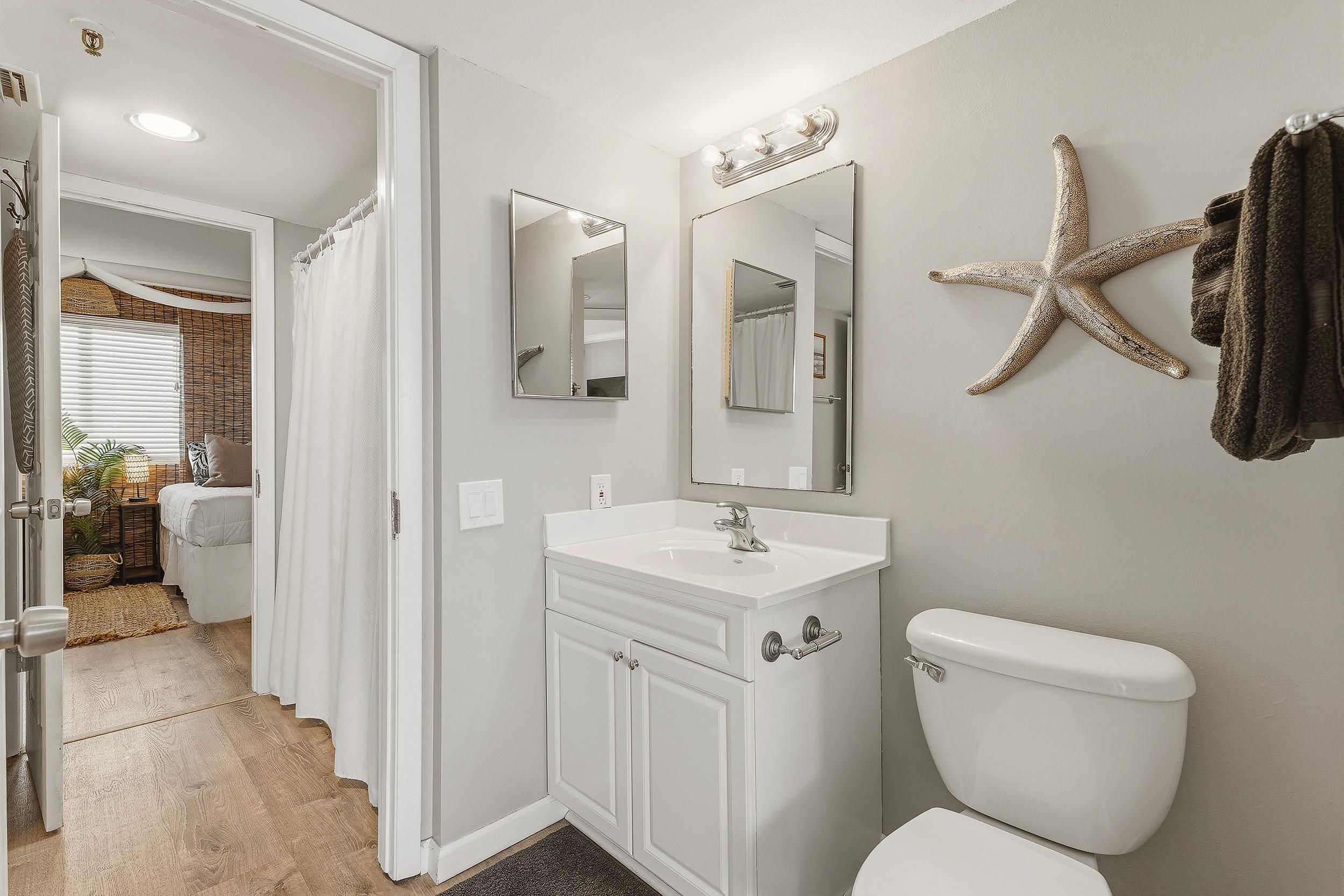 Ein Badezimmer mit weißem Waschtisch, Toilette, Spiegel und einer Meerstern-Dekoration an der Wand.