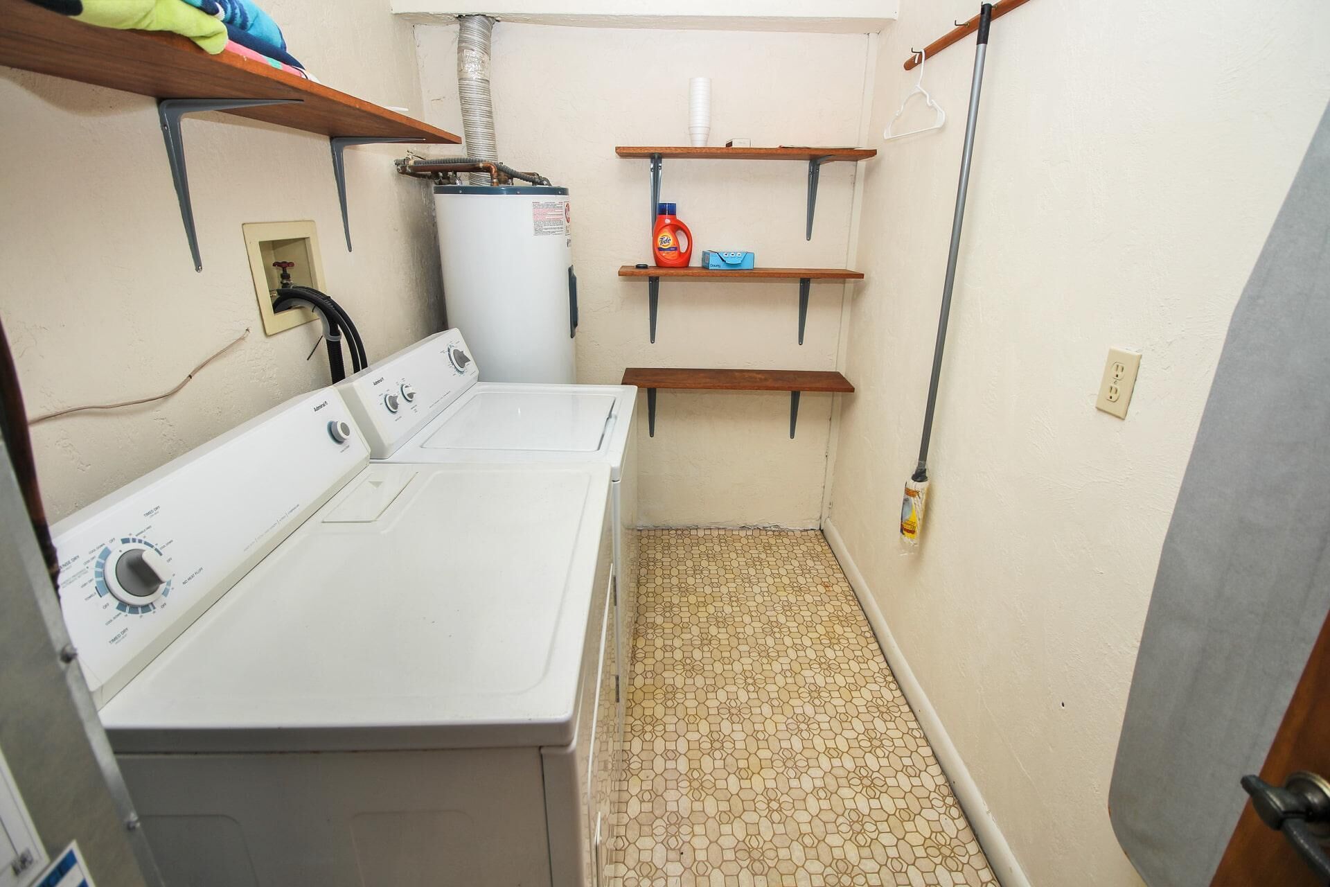 A laundry room with a washing machine, shelves with cleaning supplies, and a mop.