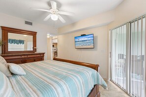 A bedroom with a bed, a ceiling fan, a TV, and a sliding glass door to a balcony. - Oceanwalk 1-203 (New Smyrna Beach)