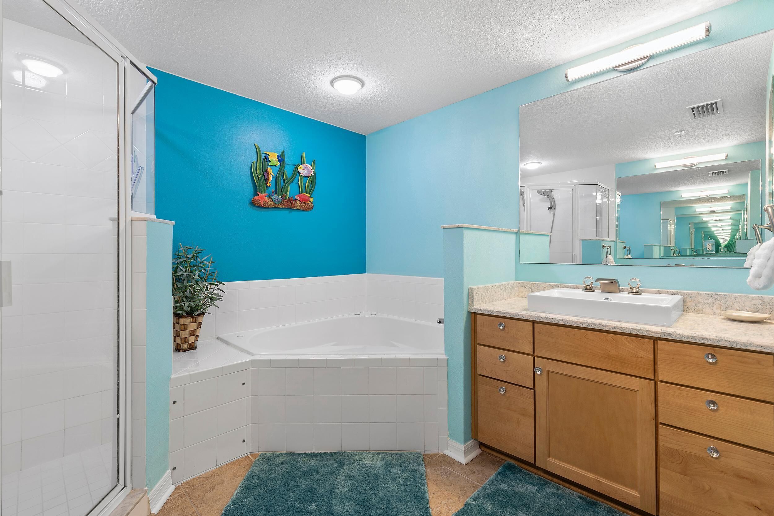 A bathroom with a white bathtub, a sink with a mirror above it, and a blue wall with a cactus decoration.