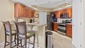 A kitchen with wooden cabinets, stainless steel appliances, and a bar area with two chairs. - Oceanwalk 13-406 (New Smyrna Beach)