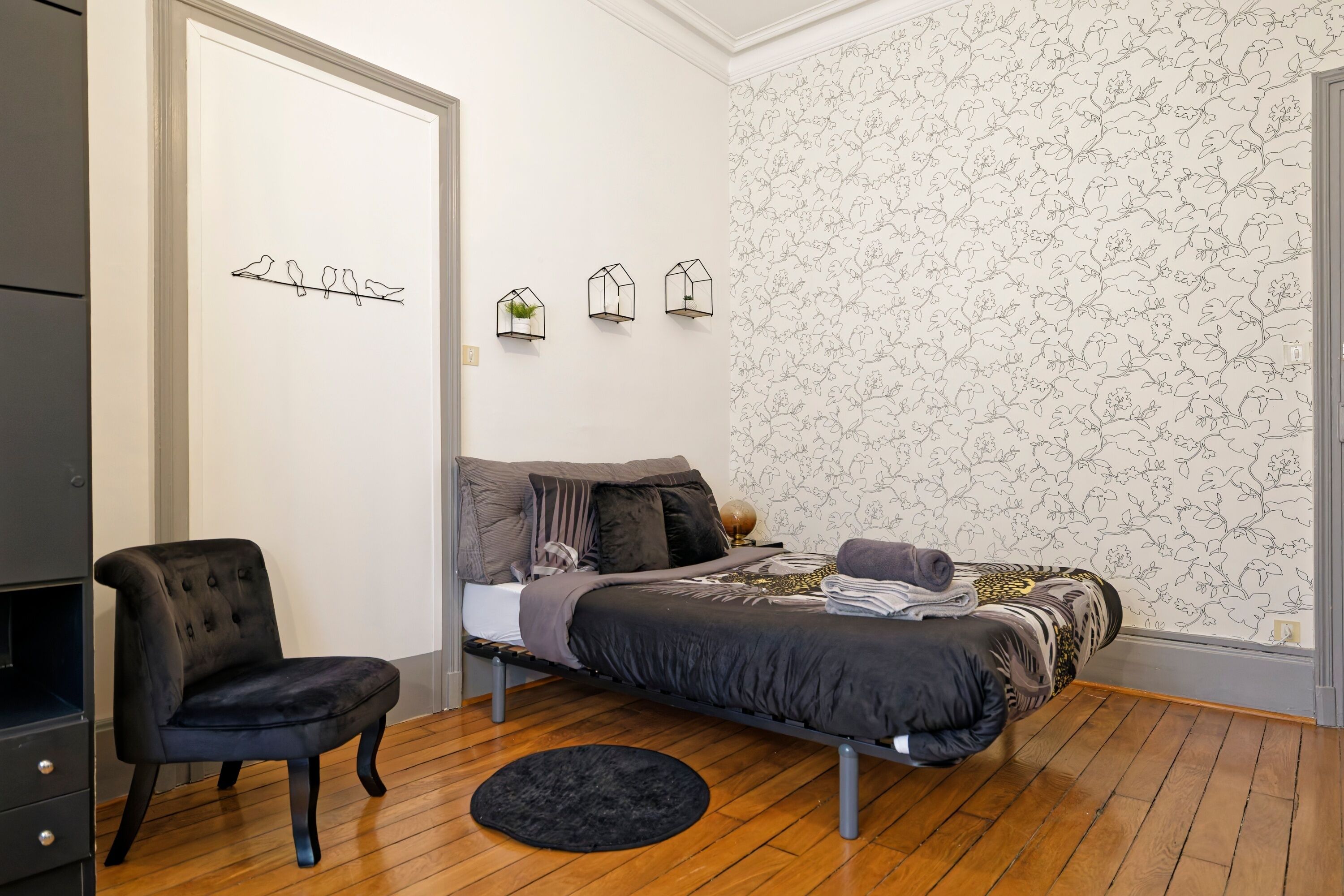 A bedroom with a bed, a chair, a dresser, and a wall with bird and house decorations.