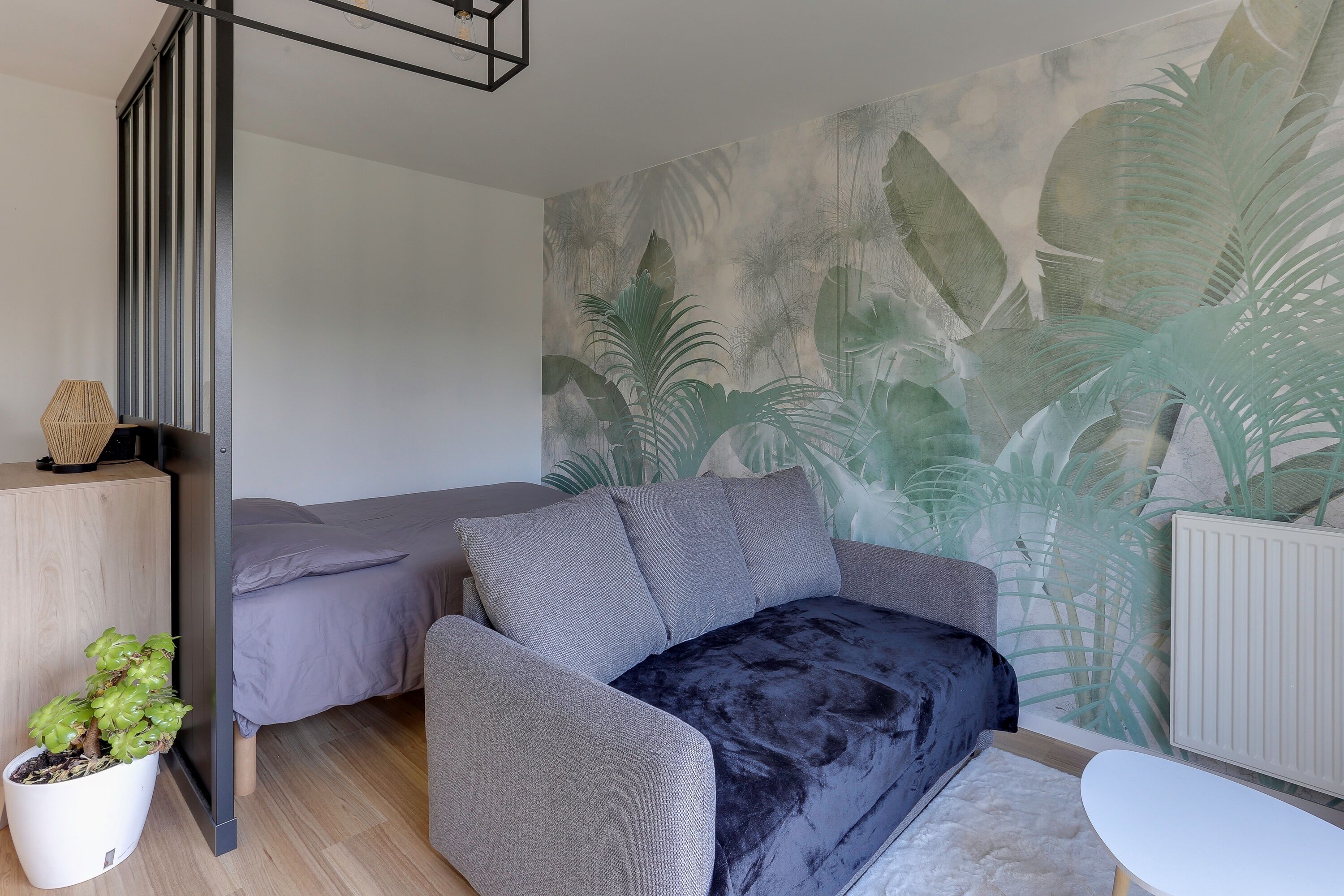 Un salon moderne avec un canapé gris, une petite table blanche et une plante en pot.