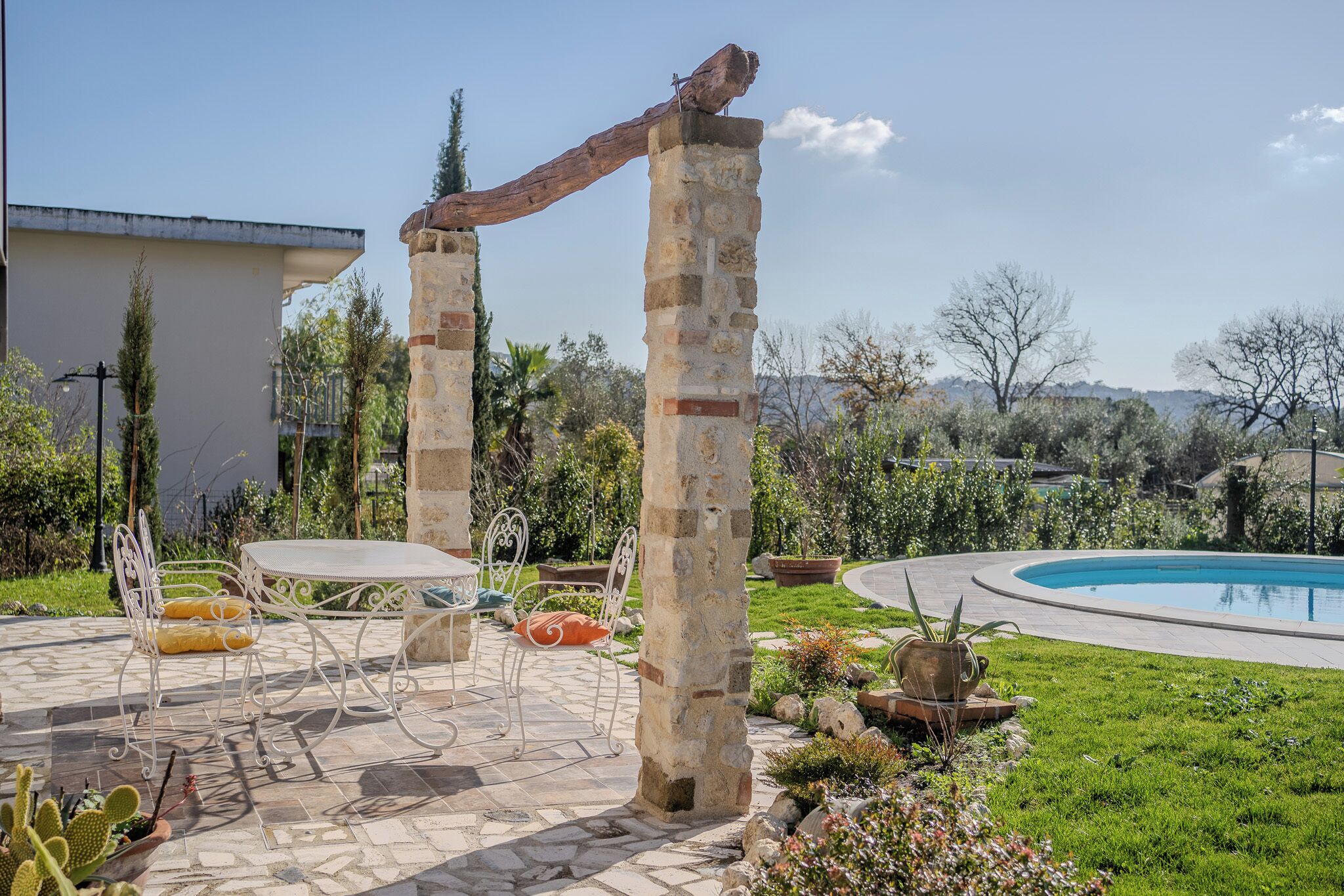 A patio with stone pillars, a pool, and outdoor furniture.