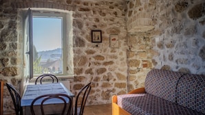 Una habitación con paredes de piedra, una mesa de comedor y sillas, un sofá estampado y un ventanal con vistas.