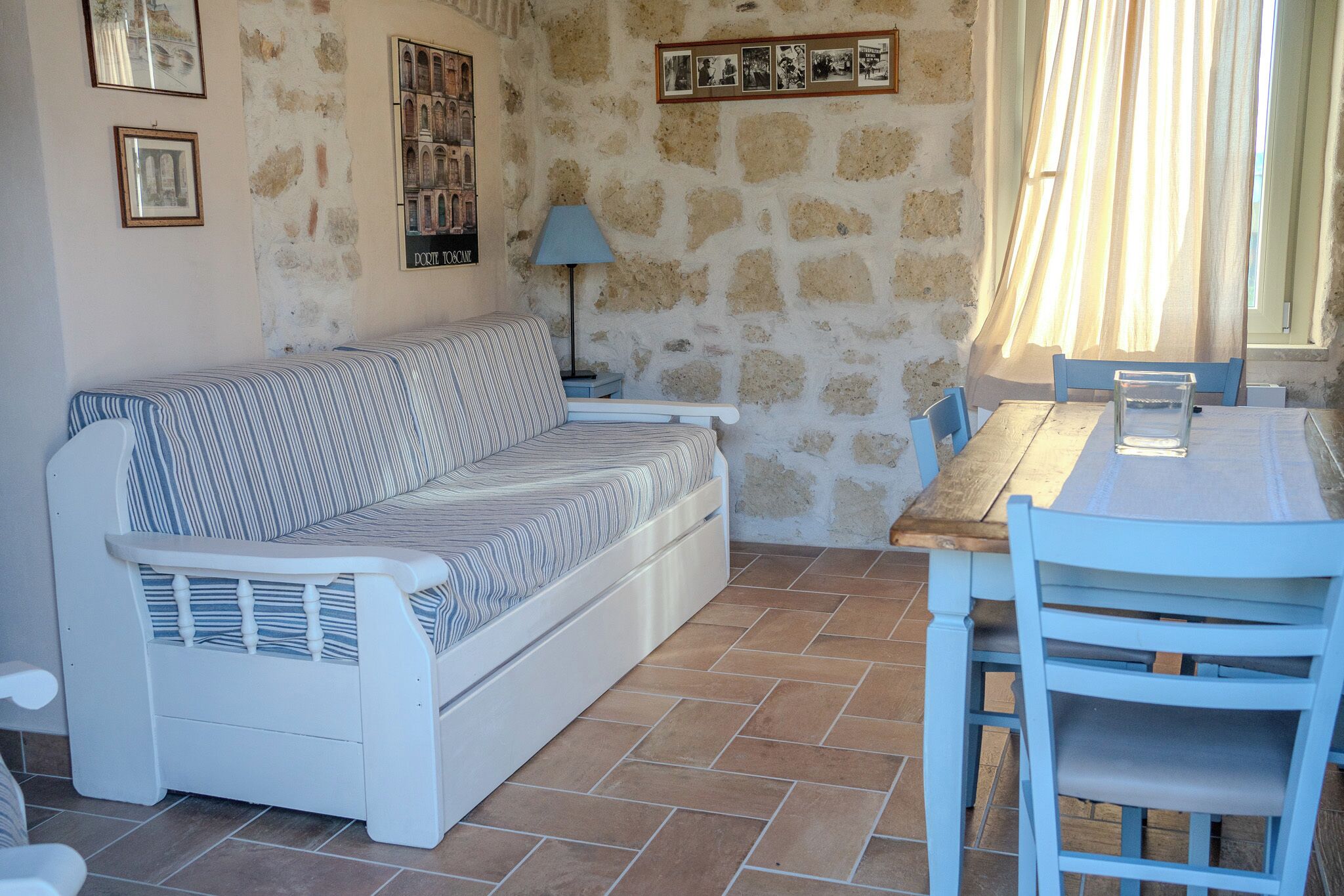 A room with a stone wall, a striped sofa, a wooden table, and chairs.