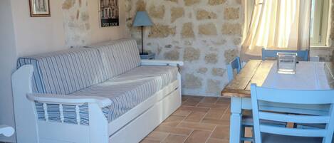 A room with a stone wall, a striped sofa, a wooden table, and chairs.