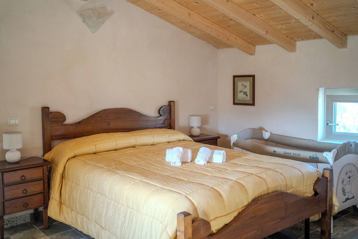 A bedroom with a wooden bed, a bedside table, a nightstand, a window, and a framed picture on the wall.