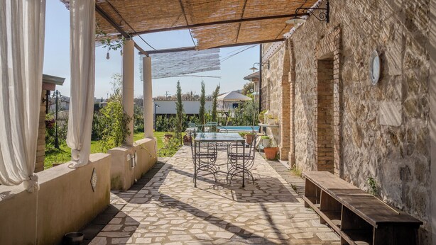 Un patio techado al aire libre con piso de piedra, una mesa con sillas y un banco.