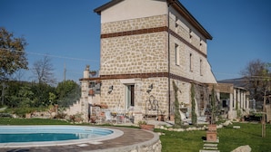 Un edificio de piedra con piscina, mobiliario exterior y jardín.