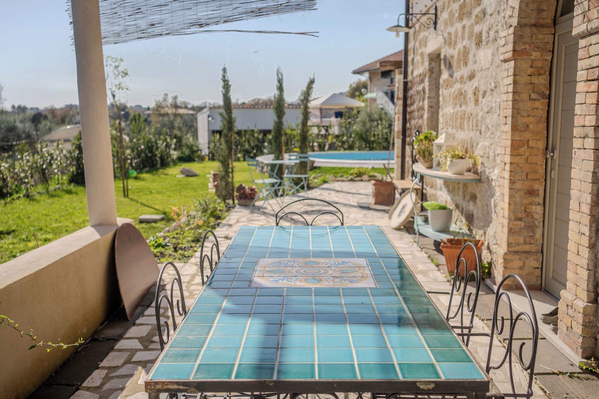 An outdoor patio with a tiled table and chairs, surrounded by a stone wall and potted plants.