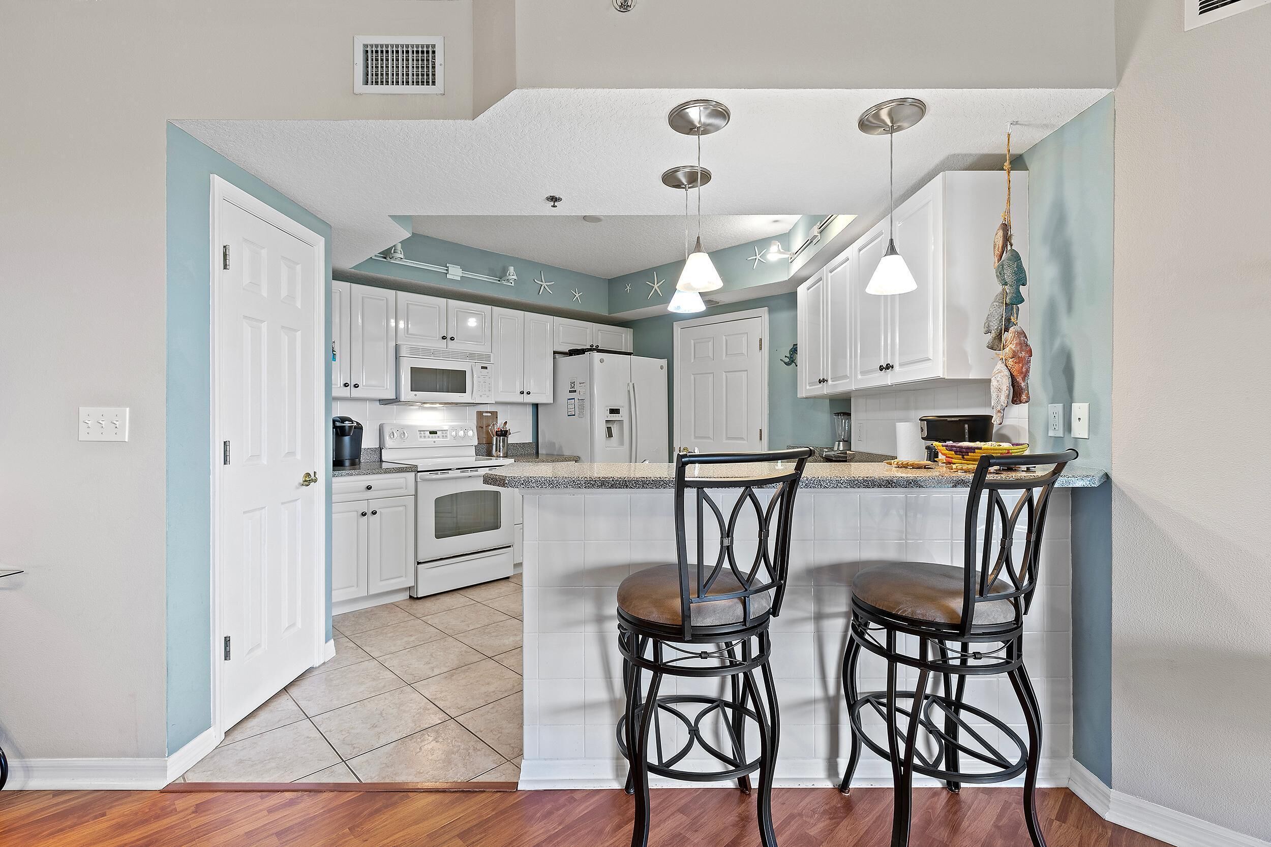 A kitchen with white cabinets, a central island with two bar stools, and a hanging light fixture.