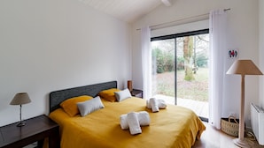 Ein Schlafzimmer mit einem großen Bett, einem Nachttisch, einer Lampe und Blick ins Freie.