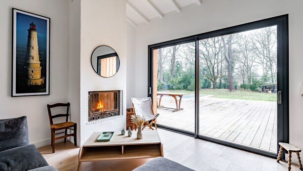 Ein modernes Wohnzimmer mit Kamin, großem Fenster und Blick auf eine Terrasse.