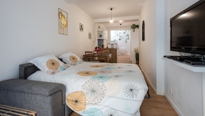 A modern bedroom with a large bed, a grey sofa, a TV, and a dining area in the background. - Rosamel - Studio à 1km de la gare, proche port (Etaples-sur-Mer)