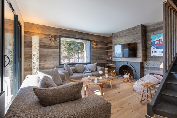 A modern living room with a fireplace, wooden walls, and a large window.