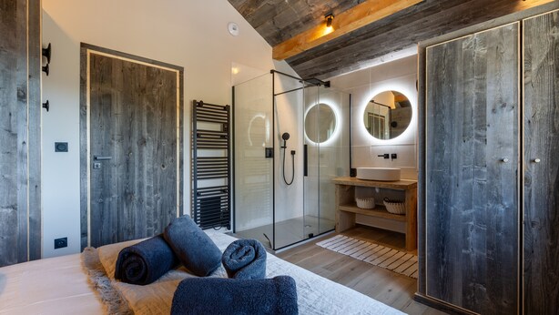 Un dormitorio moderno con una cama grande, cabina de ducha con paredes de vidrio y detalles de madera.