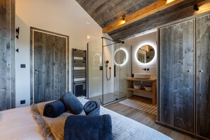 A modern bedroom with a large bed, a glass-enclosed shower, and wooden accents.