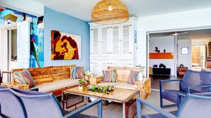 A living room with a wooden sofa, blue chairs, a wooden coffee table, and a large painting on the wall.