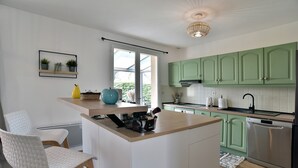 A modern kitchen with green cabinets, a white island, and a window overlooking greenery.