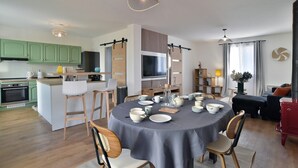 A modern kitchen with green cabinets, a dining area with a round table, and a living space with a red cabinet and a TV.