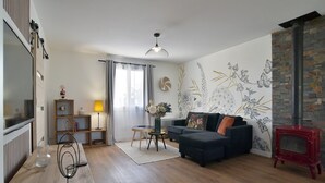 A modern living room with a dark sofa, a small round table with a vase, a wooden floor, a red fireplace, and a wall with botanical illustrations.