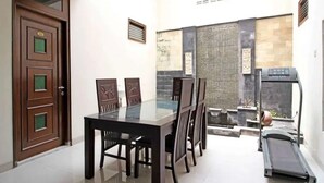 Un espace repas avec une table et des chaises à plateau en verre, un tapis de course et un mur en pierre agrémenté d’un élément décoratif aquatique.