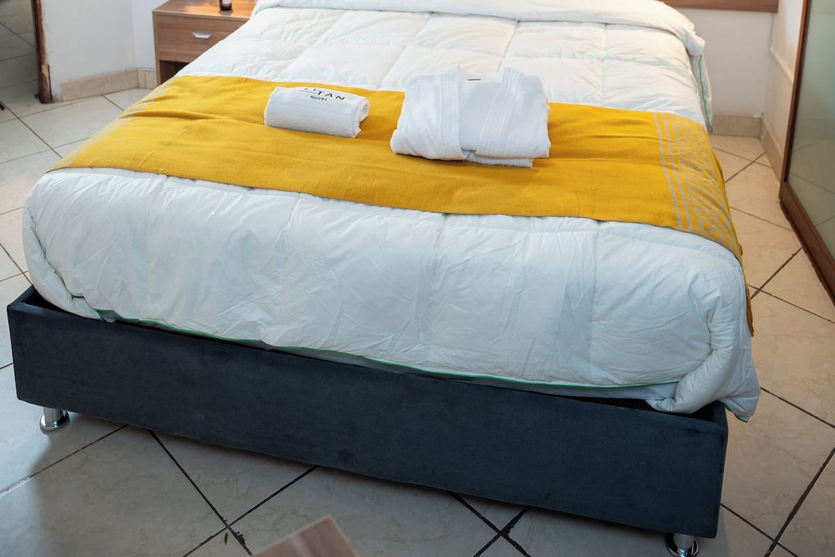 A modern hotel room with a large bed, a bedside table with a vase of flowers, and a wall-mounted air conditioner.