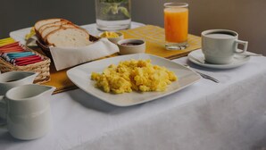 A breakfast table with bread, scrambled eggs, a glass of orange juice, and a cup of coffee, with a view of buildings and a mountain in the background. - HOTEL LITAN (Cusco)