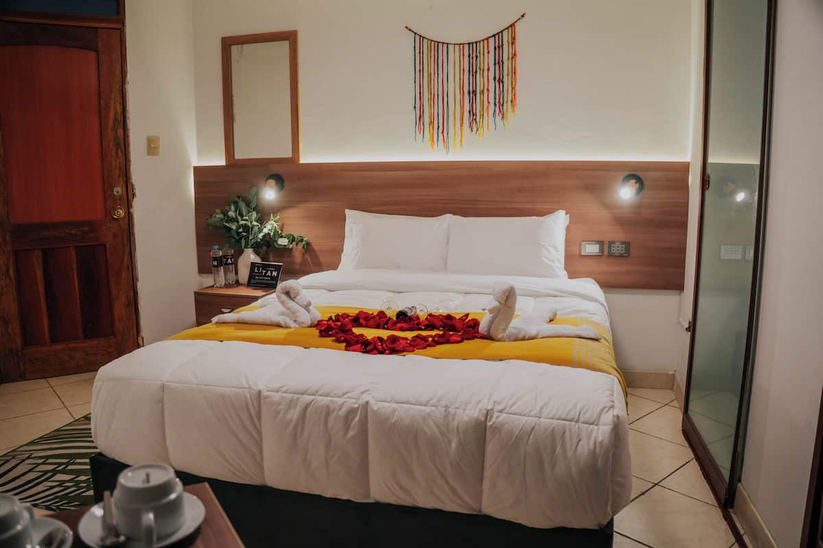 A hotel room with a wooden headboard, a bed with white bedding, a yellow throw blanket, and a decorative wall hanging.