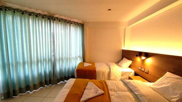 A hotel room with two beds, a wooden headboard, a bedside table, and a window with curtains. - HOTEL LITAN (Cusco)