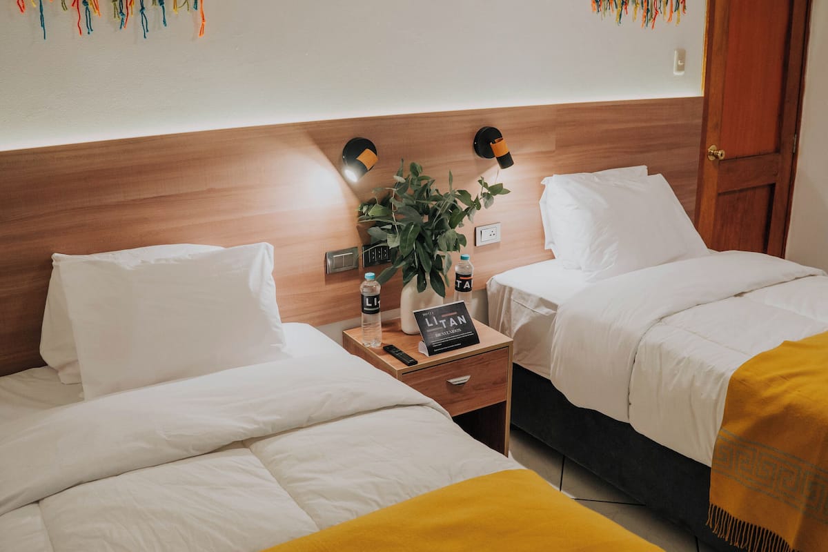 A hotel room with two beds, a wooden headboard, a nightstand with a plant, and a sign.