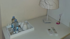 Escritorio blanco con una lámpara, un atril con botellas de agua y una taza, dos cuadros coloridos y un cartel con detalles de Wi-Fi.